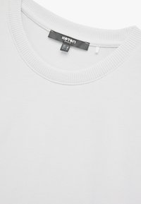 Sudadera blanca de cuello redondo con ribete en el cuello. La tela parece suave y texturizada, con una etiqueta que muestra el nombre de la marca y la información de cuidado.