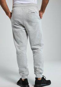 Grå bomulds sweatpants med ribbede manchetter, elastisk talje og en baglomme. Har et diskret logo broderet på ryggen.