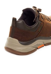 Pruun nahast ja võrguga nike, halli ja beeži tallaga, millel on pruuni tooni aktsendid ja tekstureeritud kanna jaoks parem haardevõime.