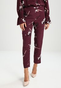 Pantalones de flores burdeos con un corte ajustado, que presentan diseños de flores en blanco y negro, confeccionados en un tejido ligero, combinados con tacones beige.