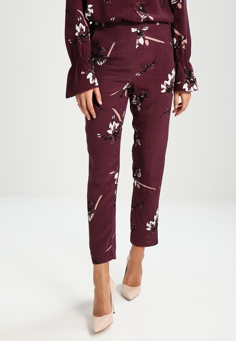 Pantalones de flores burdeos con un corte ajustado, que presentan diseños de flores en blanco y negro, confeccionados en un tejido ligero, combinados con tacones beige.