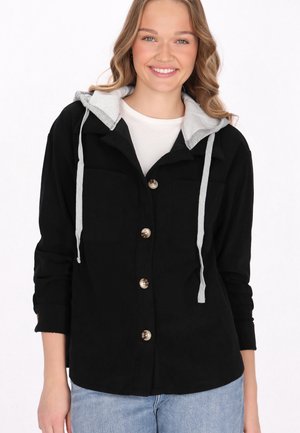 Zwarte corduroy overhemdjas met een grijze hoodie, met knoopsluitingen, voorzakken en opgerolde mouwen.