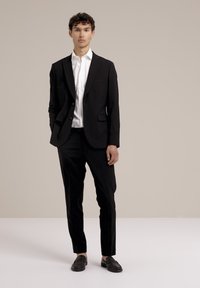 Costume noir avec un blazer à un bouton, une chemise blanche et des chaussures noires. Coupe ajustée, texture lisse et design minimaliste.