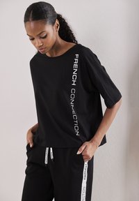 T-shirt noir en coton à manches courtes et coupe décontractée, avec "FRENCH CONNECTION" imprimé verticalement en blanc sur le côté gauche.