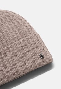 Gestrickte Mütze in Hellbeige mit geripptem Bündchen. Besitzt ein kleines, metallisches Logo. Weiche Textur. Runde Form. Geeignet für kaltes Wetter.