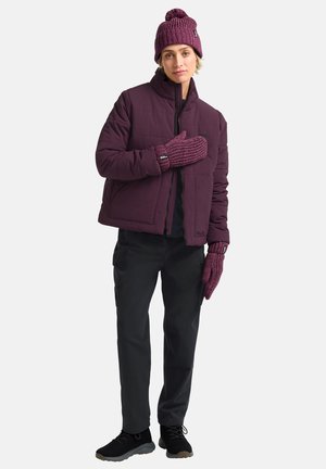 Giacca a vento bordeaux con zip frontale, abbinata a un berretto a maglia e guanti coordinati. Pantaloni neri e sneakers completano l'outfit.