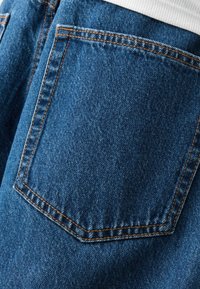 Denimtyg med en blå färg och en strukturerad yta, avslutat med orangea stygn runt en bakficka.