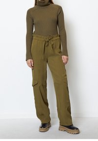 Olivově zelený žebrovaný rolák v kombinaci s olivovými cargo kalhotami s kapsami a elastickým šňůrkovým pasem, nošený s masivními černými botami.
