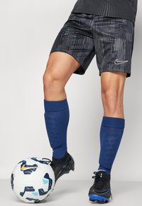 Crne Nike kratke hlače s teksturiranim uzorkom, uparene s plavim čarapama, crnim kopačkama i bijelo-plavom nogometnom loptom na stopalu.