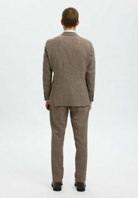 Brun rutigt kostym med en strukturerad kavaj och smala byxor. Texturerad tyg, två knappar på kavajens ärmar och eleganta svarta skor.