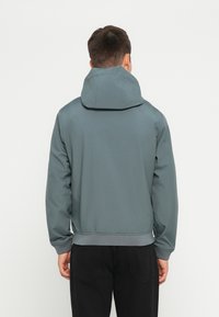 Hoodie in gedämpftem Türkis mit glatter Textur, elastischen Bündchen und einem taillierten Saum. Der Hintergrund ist rein weiß.