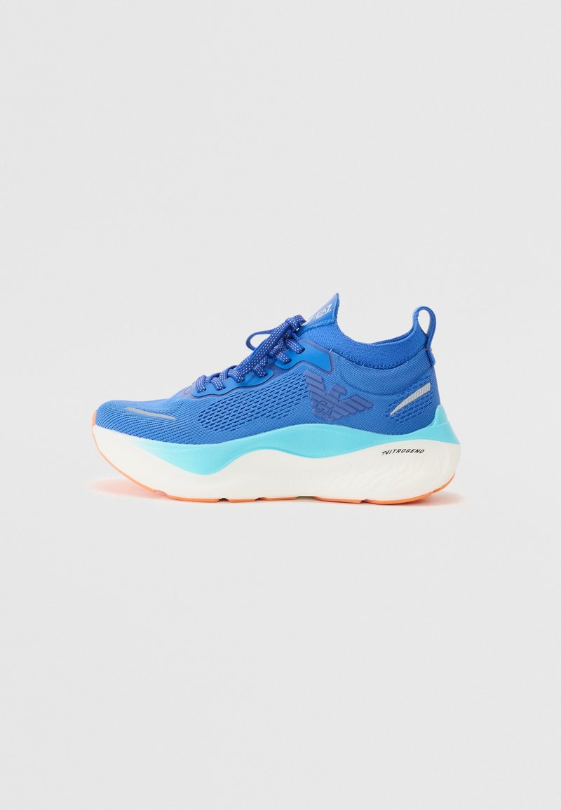 Baskets de sport bleues avec tige en mesh, semelle épaisse blanche et turquoise, design à lacets, et logo de la marque sur le côté.