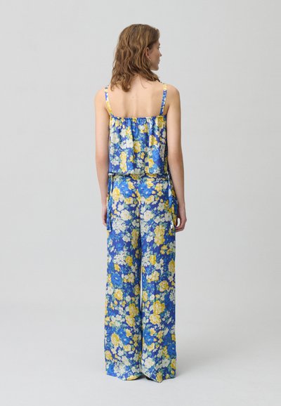 Completo floreale a due pezzi con spalline sottili. Presenta uno sfondo blu con fiori gialli e bianchi, e pantaloni larghi e comodi.