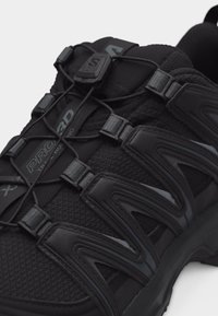 Μαύρο παπούτσι για τρέξιμο σε μονοπάτι με άνω μέρος από δίχτυ, συνθετικά επικάλυψη, σύστημα γρήγορου δέσιμου και διακριτικό με την ένδειξη «PRORAD» στο πλάι.