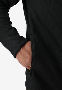 Maglia nera a maniche lunghe con texture e tasca laterale con zip. Il tessuto presenta un motivo a griglia e polsini rigati.