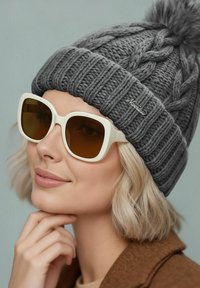 Gray knitted beanie with a fur pom-pom, featuring a cable-knit pattern. White oversized sunglasses with brown lenses add contrast.