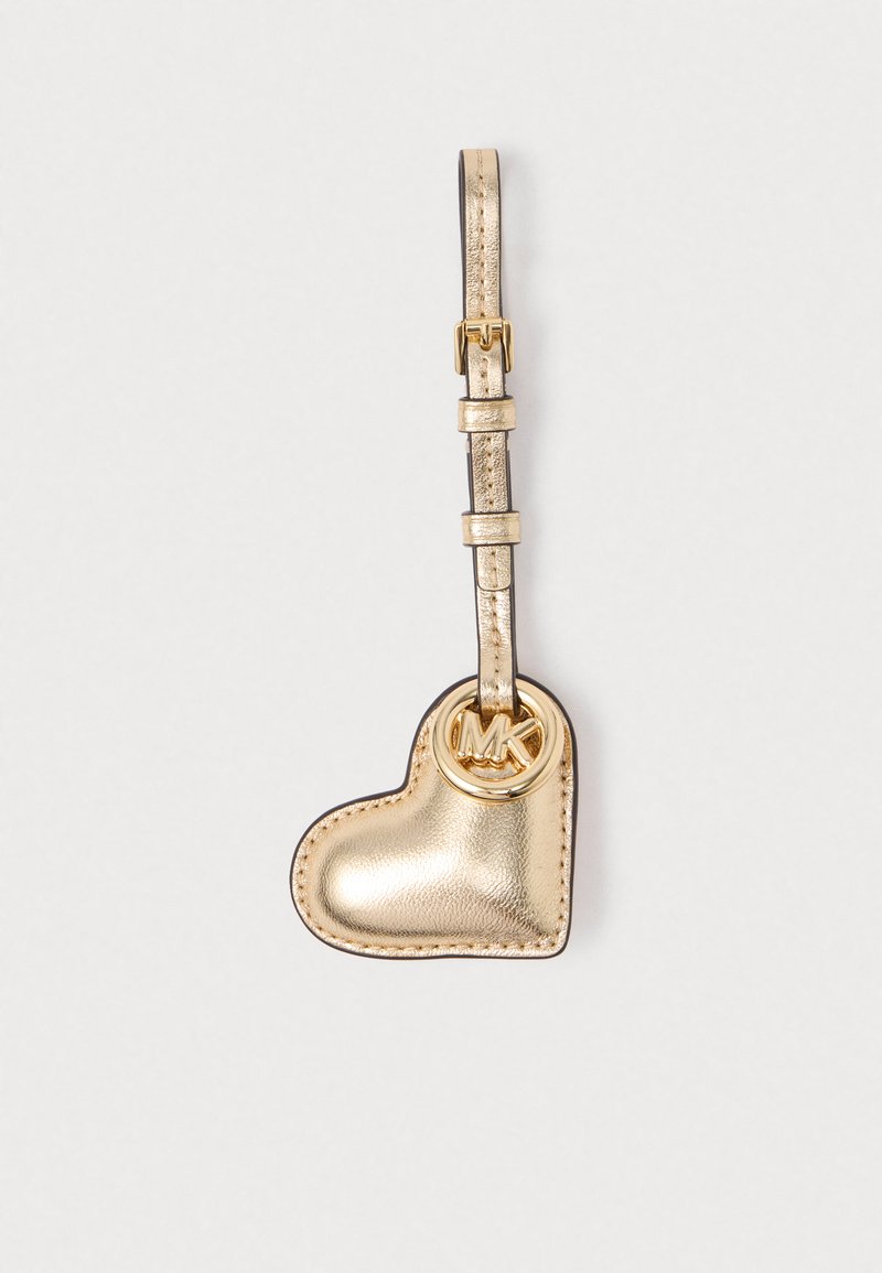 Portachiavi in pelle a forma di cuore metallico dorato con cinturino regolabile e charm con logo MK dorato su uno sfondo bianco semplice.