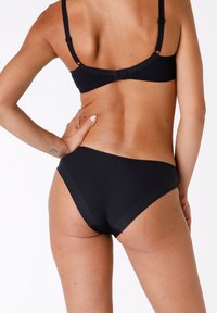 Set di bikini nero con un design semplice, tessuto dalla superficie liscia e spalline regolabili. La vista posteriore mostra una copertura minima con linee pulite.