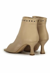 Stivali ankle in pelle beige con punta aperta, decorati con perline circolari lungo il bordo superiore, dotati di un tacco basso e svasato.