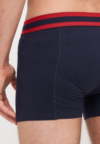 Des boxers en coton bleu marine avec une ceinture rayée rouge et bleue, présentant une texture lisse et un design ajusté.