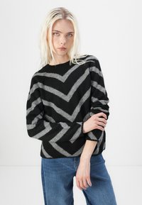 Musterniga mustri ja halli triibuline chevron-krae, ümarate kaelustega ja pikkade varrukatega kampsun, mis on valmistatud pehmest tekstuuriga kangast.