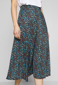 Floraler Midirock in Schwarz mit verstreuten blauen, roten und weißen Mustern. Mit hohem Bund und fließendem Saum. Hergestellt aus leichtem Stoff.