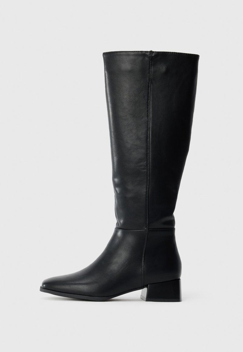 Bota preta de couro até ao joelho com tacão baixo e bico fino, mostrada de lado sobre um fundo claro e liso.