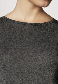 Pull noir avec une texture fine et scintillante, doté d'un col large et d'un ourlet côtelé simple.