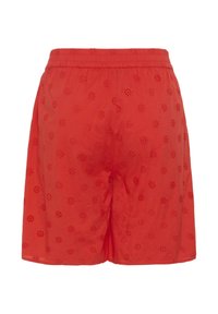 Short rouge avec taille élastique, orné de petits motifs floraux découpés répartis uniformément sur le tissu.