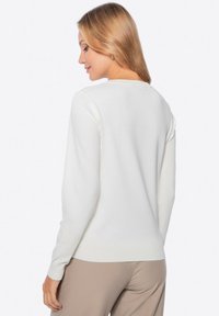 Maglione bianco a maniche lunghe con scollo rotondo, polsini e orlo a costine. Realizzato in un morbido tessuto a maglia con una consistenza liscia.