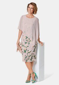 Rosa Kleid mit floralen Mustern, kurzen Cape-Ärmeln und knielanger Schnittform. Kombiniert mit türkisfarbenen High Heels und einer metallischen Clutch.