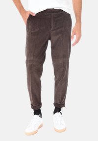 Pantaloni in velluto a coste marroni con texture a righe verticali, dotati di chiusura a bottone e orli arrotolati, abbinati a sneaker bianche.