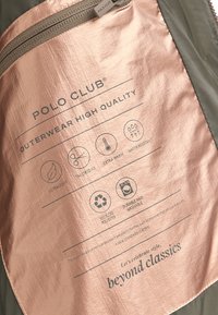 Textiletikett från en jacka med bakgrund i metallisk roséguld, svart text och ikoner som beskriver skötsel, material och egenskaper.