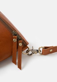 Brown leather bag with a zipper, featuring brass hardware, double zipper pulls, and a detachable strap with a snap hook.
