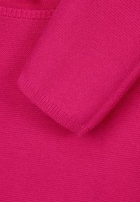Tejido de punto fucsia con una textura suave, que presenta un puño acanalado y un diseño sin costuras. Primer plano que muestra una costura uniforme y un color vibrante.