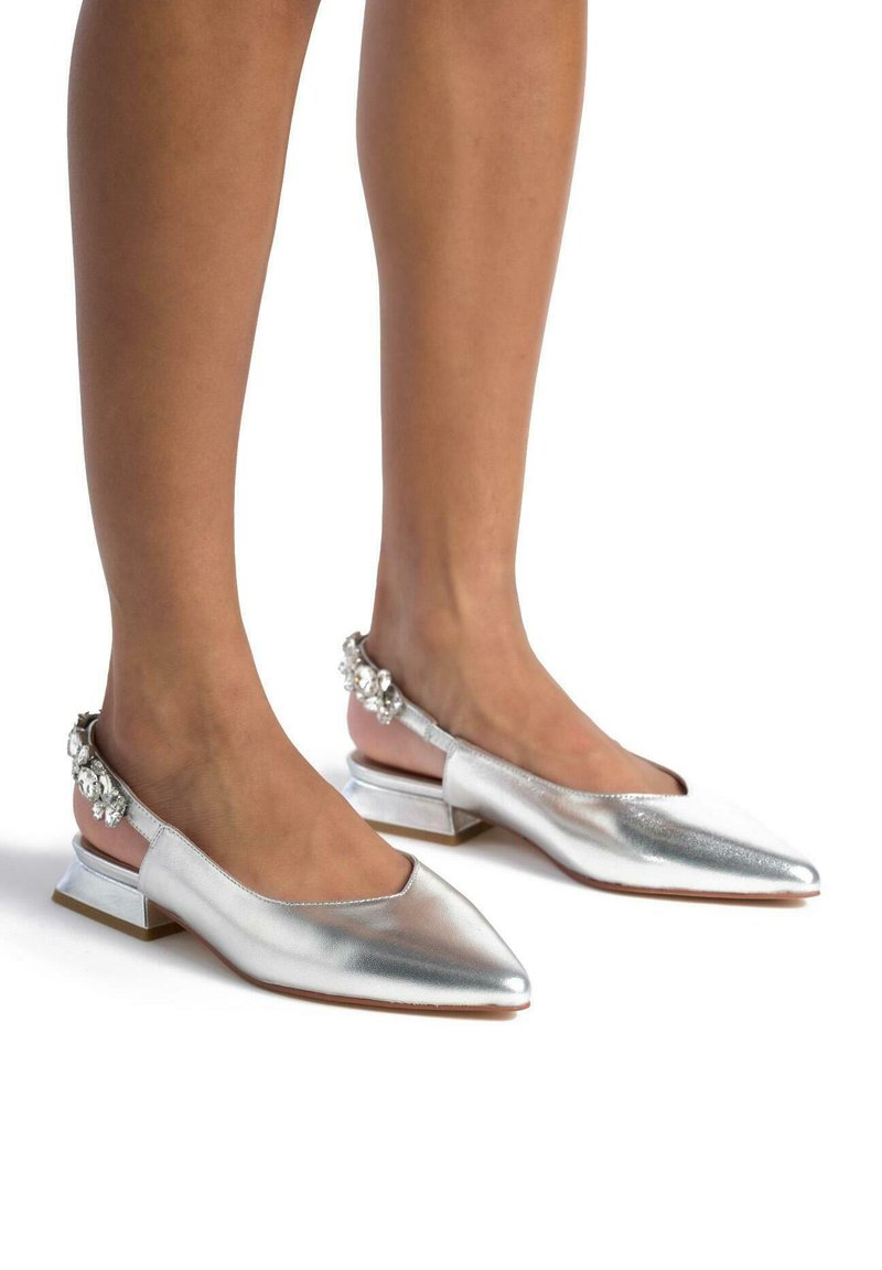Scarpe slingback metalliche argento con punta affilata e tacco basso a blocco, decorate con accenti di cristallo sul retro. Texture liscia.