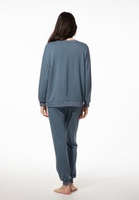 Twee-delig lounge set in zacht, gedempt blauw stof. Langsleevetop met een relaxte pasvorm, bijpassende tapershorts met geribbelde manchetten. Gladde textuur.