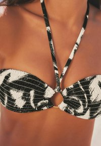 Fekete-fehér mintás bikini felsőrész, bandeau fazonnal, középen arany gyűrűvel és vékony állítható pántokkal. Textúrált anyag.