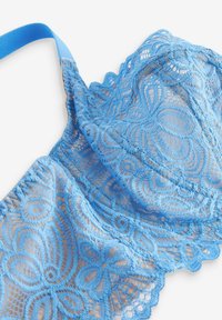 Reggiseno blu in pizzo con motivi floreali, bordi scallop e spalline regolabili, realizzato in un materiale delicato e trasparente.