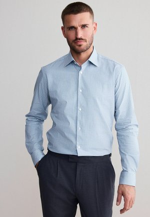 Light blue checkered dress shirt with a structured collar, long sleeves, and white buttons, paired with dark gray trousers.