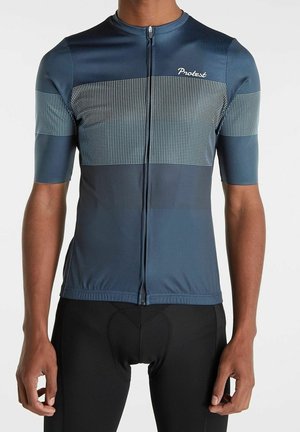 Homme portant un maillot de cyclisme bleu marine avec des rayures horizontales blanches en pointillé et une fermeture éclair à l'avant, associé à un cuissard de cyclisme noir rembourré.