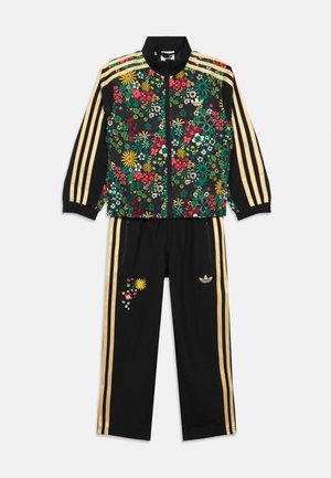 Schwarzer Trainingsanzug mit goldenen Streifen, Blumendruck auf der Vorderseite der Jacke und am linken Hosenbein, Jacke mit durchgehendem Reißverschluss, elastische Bündchen und Adidas-Logos.