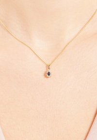 Collier en chaîne dorée avec une pierre précieuse bleue ovale entourée d'un halo de petites pierres claires, montée sur une chaîne délicate.