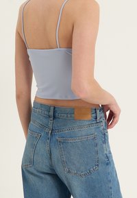 Světlý modrý cropped top vyrobený z hladké látky, spárovaný s vysokými světle modrými džíny, které mají koženou nášivku a zadní kapsy.