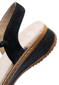 Zwarte suède sleehaksandaal met beige gevoerde binnenzool met label "High Soft" en een zwart rubberen zool met een bruine rand en textuur.