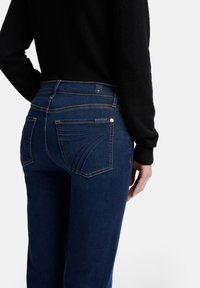 Dunkelblaue Denim-Jeans mit figurbetonter Silhouette. Verfügt über markante Gesäßtaschen mit geschwungener Naht und ein kleines Logotag nahe dem Bund.