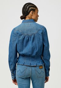 Jeansjakke i medium blå, med tilpasset midje, rynket bak og knappede mansjetter. Sammen med lyseblå jeans med sikksakk-søm.