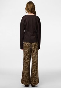 Brun långärmad topp med avslappnad passform kombinerad med högmidjade utsvängda byxor med leopardmönster i beige och svart. Mjuk textur, casual design.