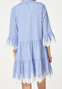 Svetle modré a bílé pruhované šaty s třičtvrtečními rukávy, volánkovým lemem a krajkovým zdobením na spodní části. Bavlněná tkanina, ležérní design.