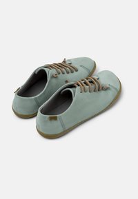 Scarpe in suede verde chiaro con lacci marroni e suola in gomma flessibile; presentano una punta arrotondata e un sottile dettaglio di cucitura.